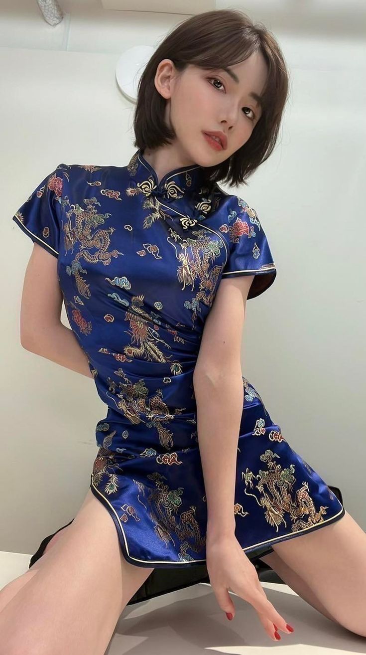 Woman in a blue cheongsam with dragon pattern and short hair posing indoors