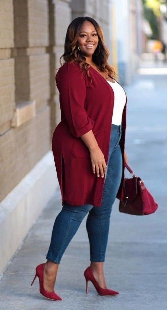 Woman in a red cardigan, blue jeans, and red heels smiling outdoors