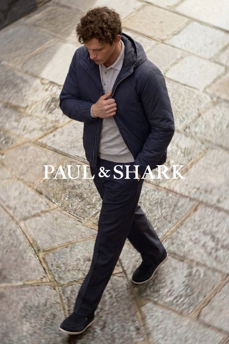 Man with curly hair in a navy jacket and polo shirt walking on cobblestone