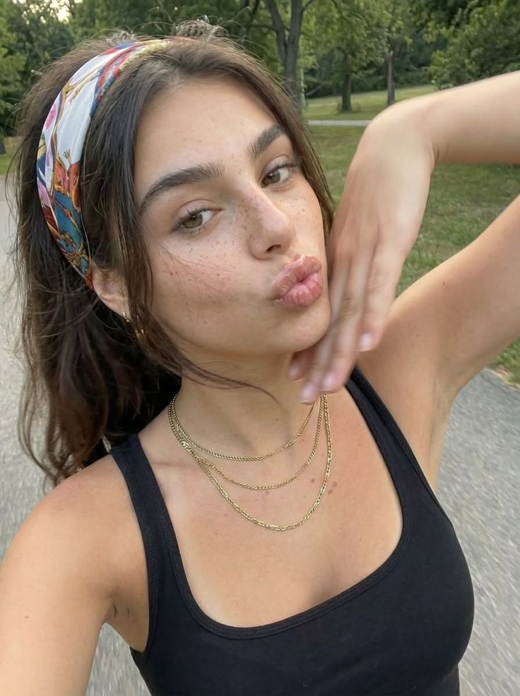 Woman with freckles and a headband wearing a black tank top and layered necklaces outdoors