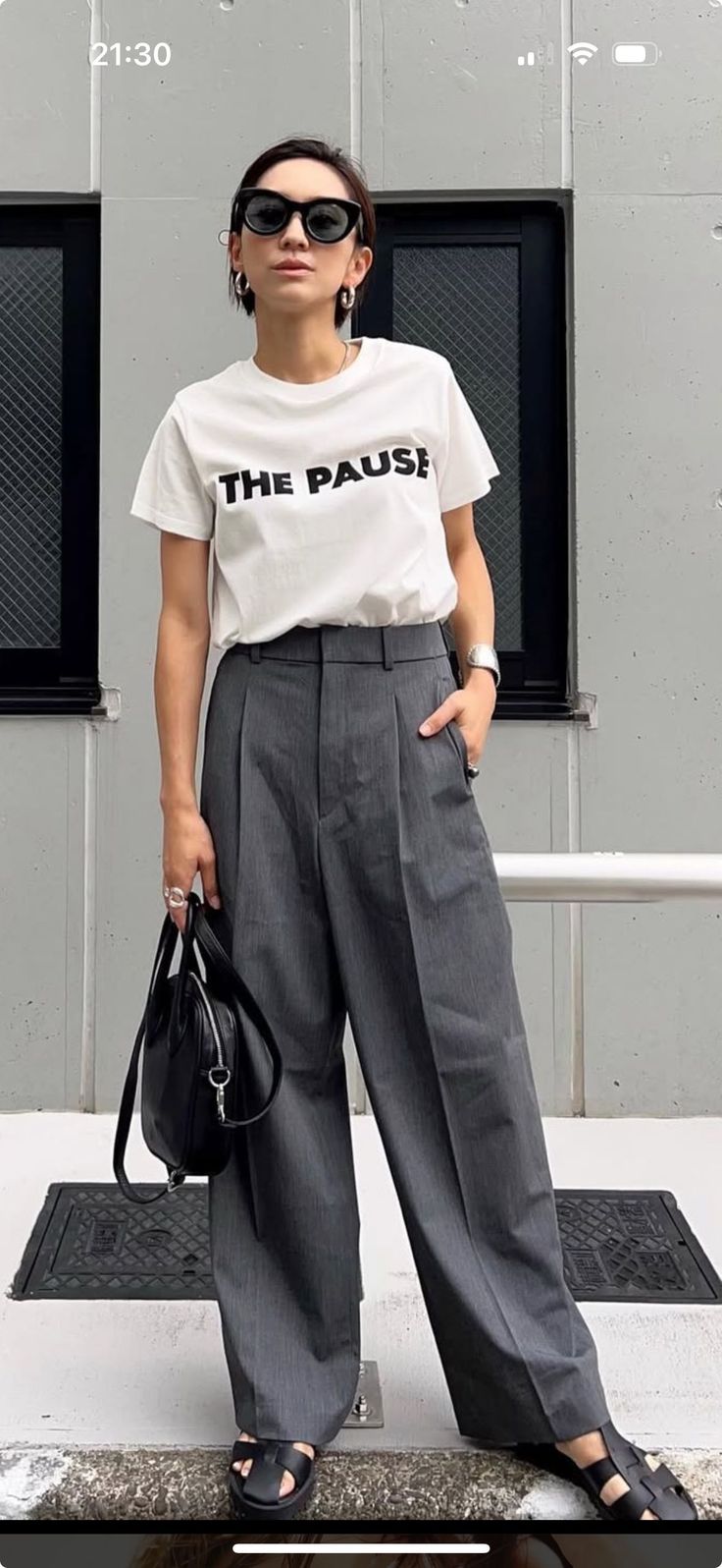 Woman in sunglasses, white t-shirt, and wide leg pants holding a black handbag