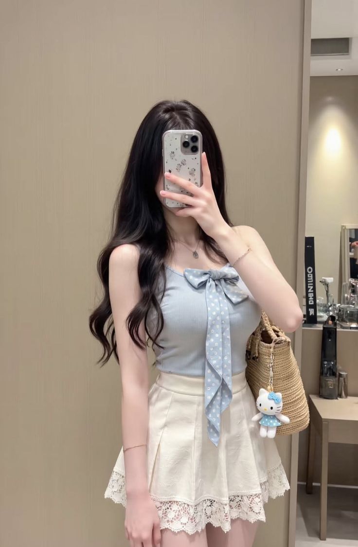 Woman with long dark hair wearing a blue top and white skirt, holding a phone