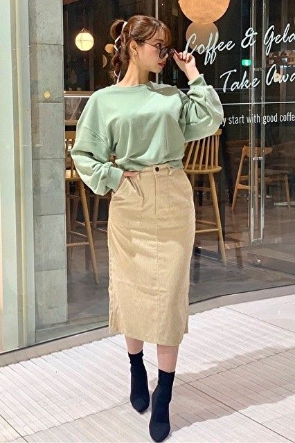 Woman in a mint green top and beige midi skirt holding sunglasses