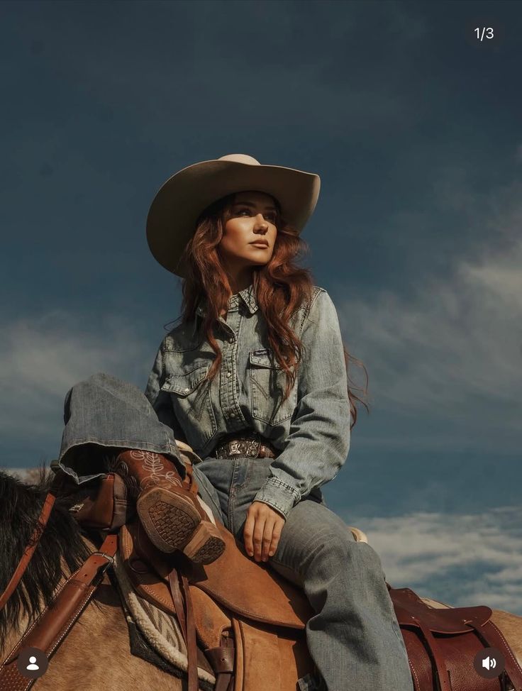 Woman in a cowboy hat and denim outfit riding a horse under a dramatic sky