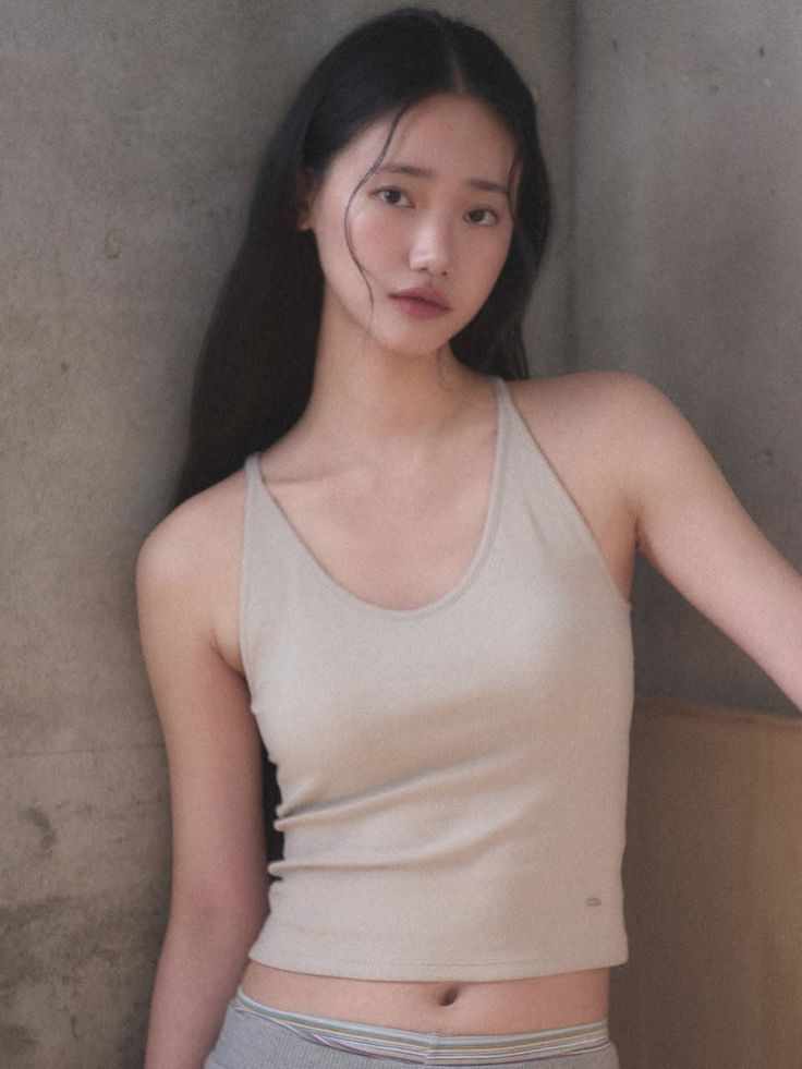 Woman with long black hair wearing a crop top and underwear, leaning against a wall