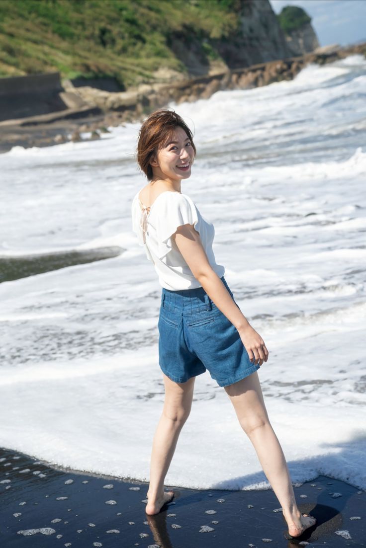 Woman with short hair in denim shorts standing on a beach with ocean waves