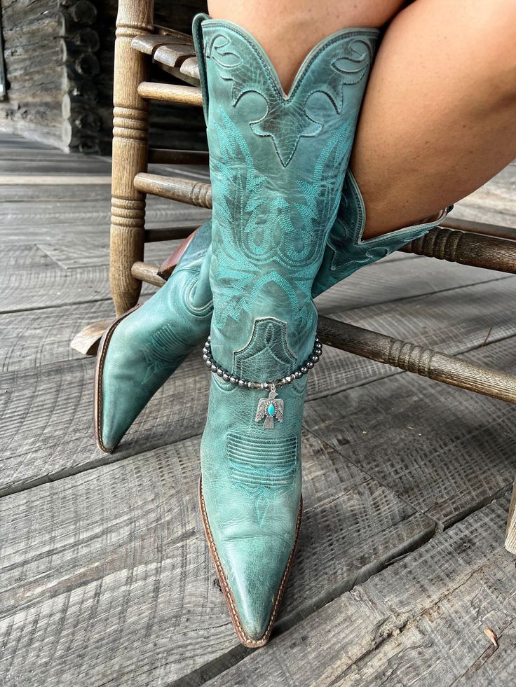 Person wearing turquoise cowboy boots with a boot bracelet on a wooden floor