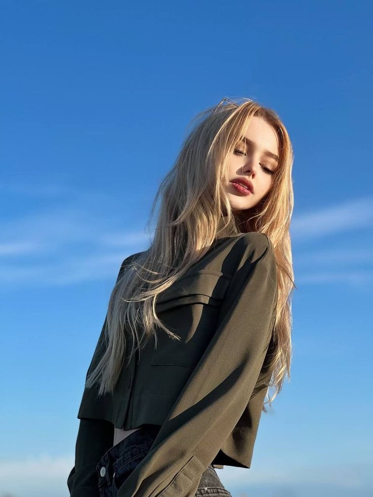 Woman with long blonde hair and a cropped jacket against a blue sky