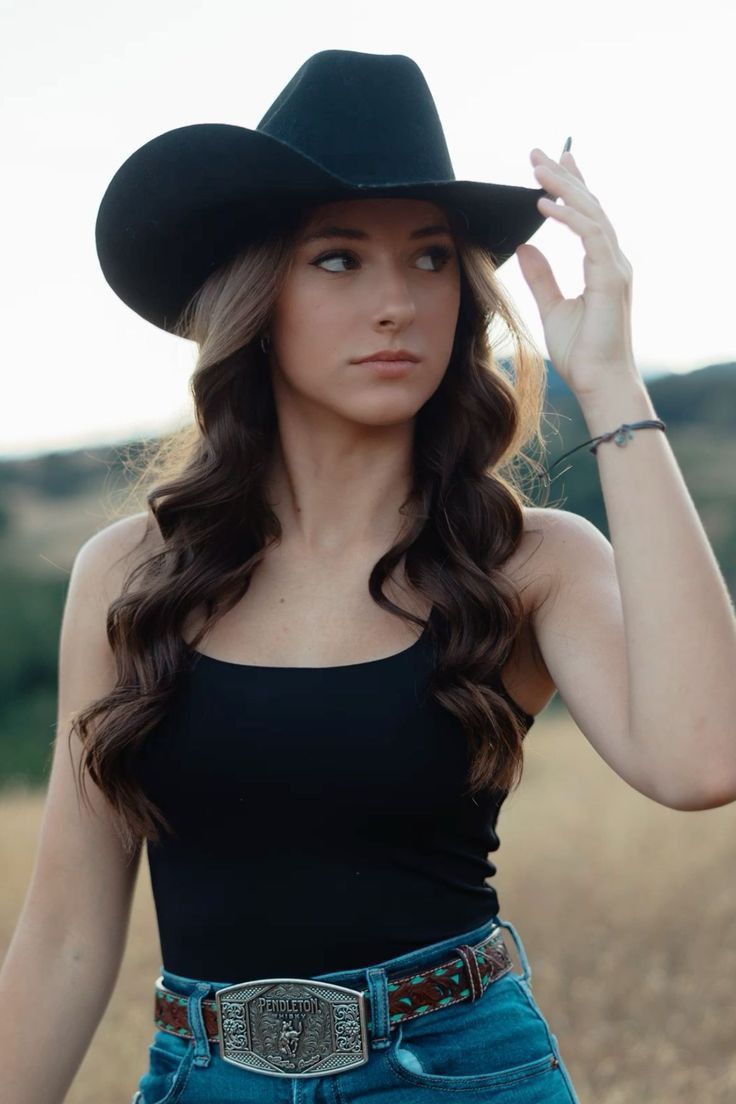 Woman in a cowboy hat and black tank top with a western belt outdoors