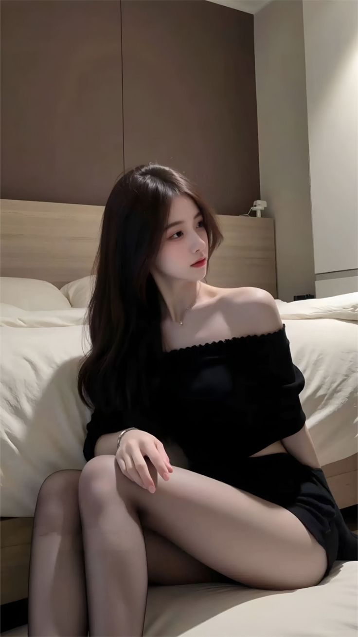 Woman with long dark hair wearing an off-shoulder top and shorts in a bedroom