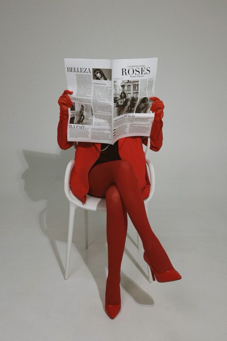 Person in a red outfit and gloves reading a newspaper while sitting on a white chair