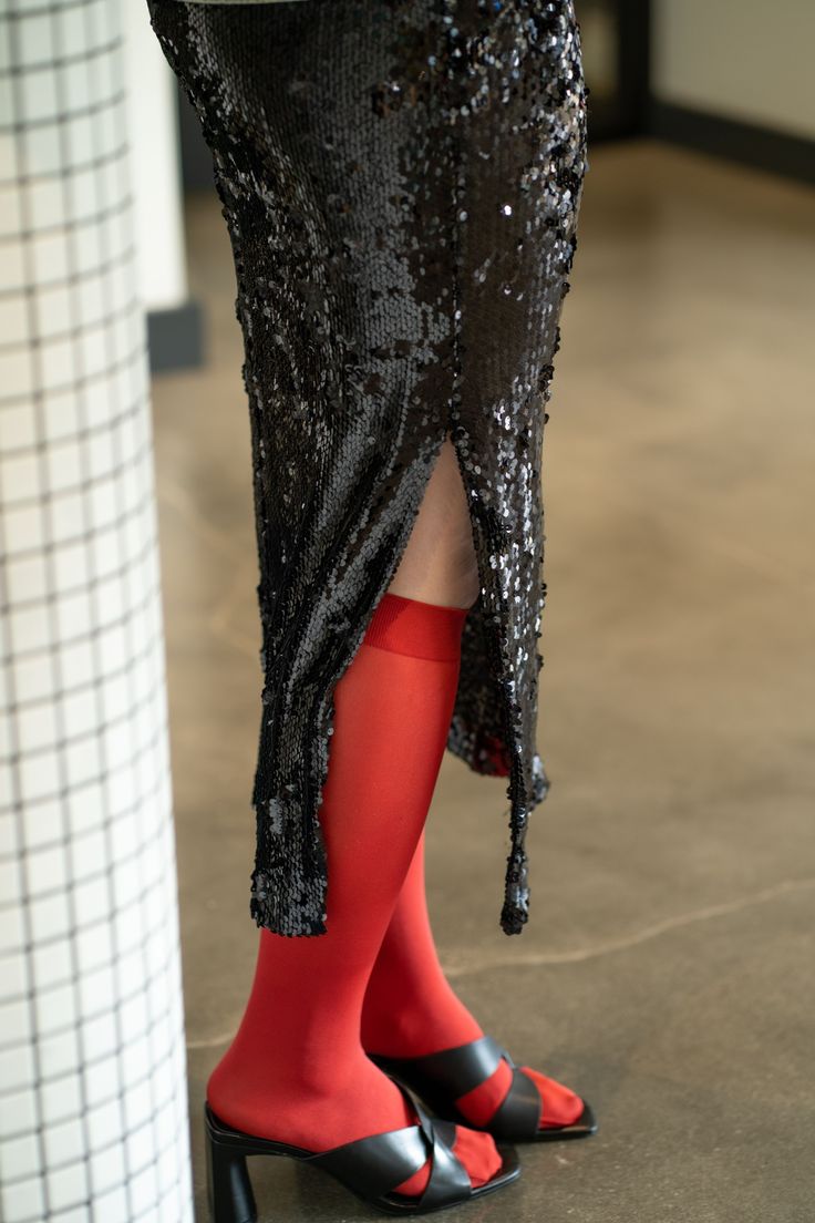 Person wearing a black sequin skirt with a split, red tights, and black heels