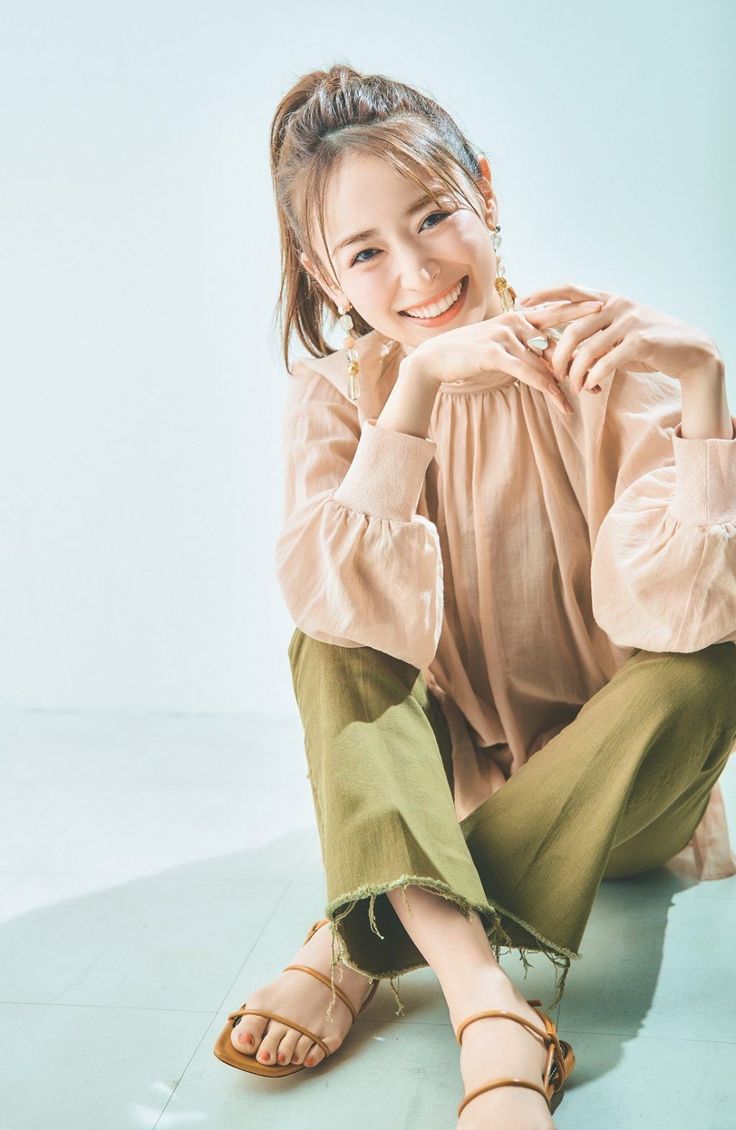 Woman with a ponytail wearing a blouse and cropped pants, sitting on the floor