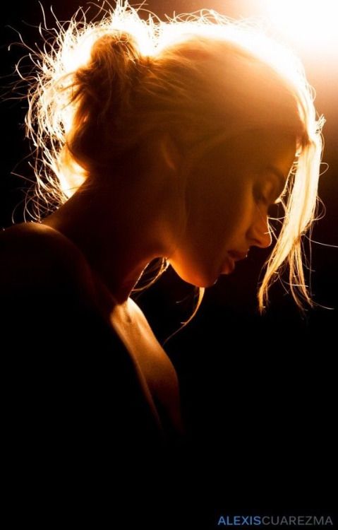 Woman with blonde hair in a messy bun, backlit against a dark background