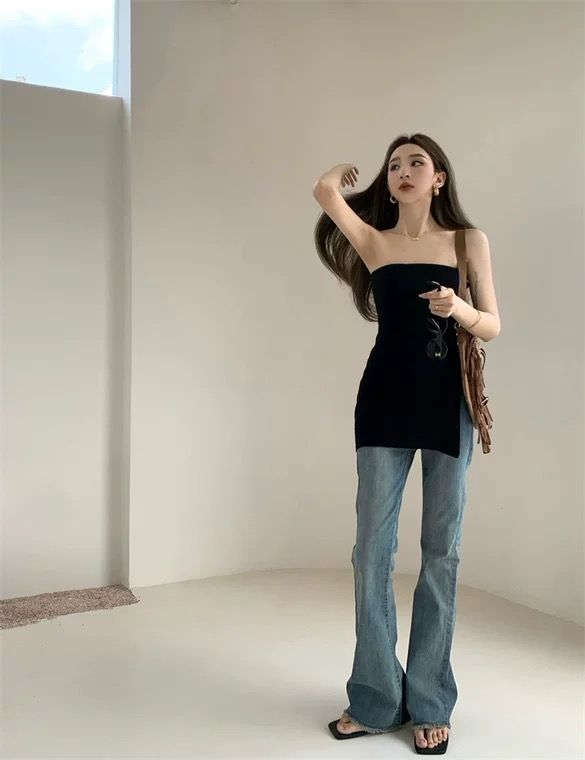 Woman in a black strapless top and flared jeans posing indoors