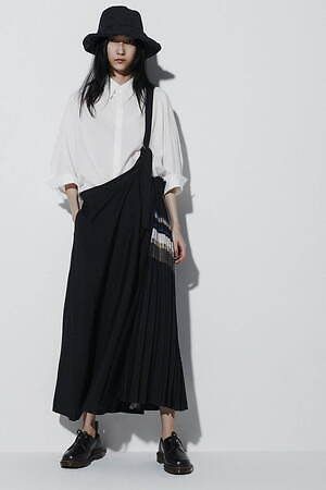 Woman in a black bucket hat, white shirt, and black pleated skirt in a studio