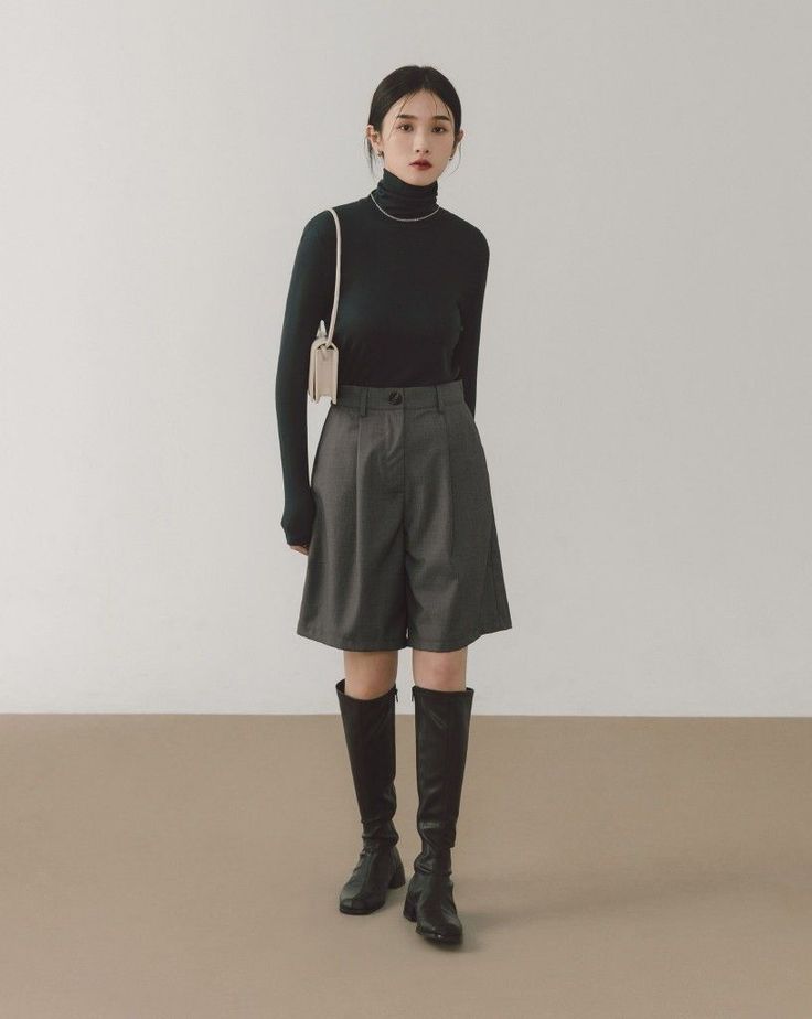 Woman in a black turtleneck, gray shorts, and knee-high boots in a studio
