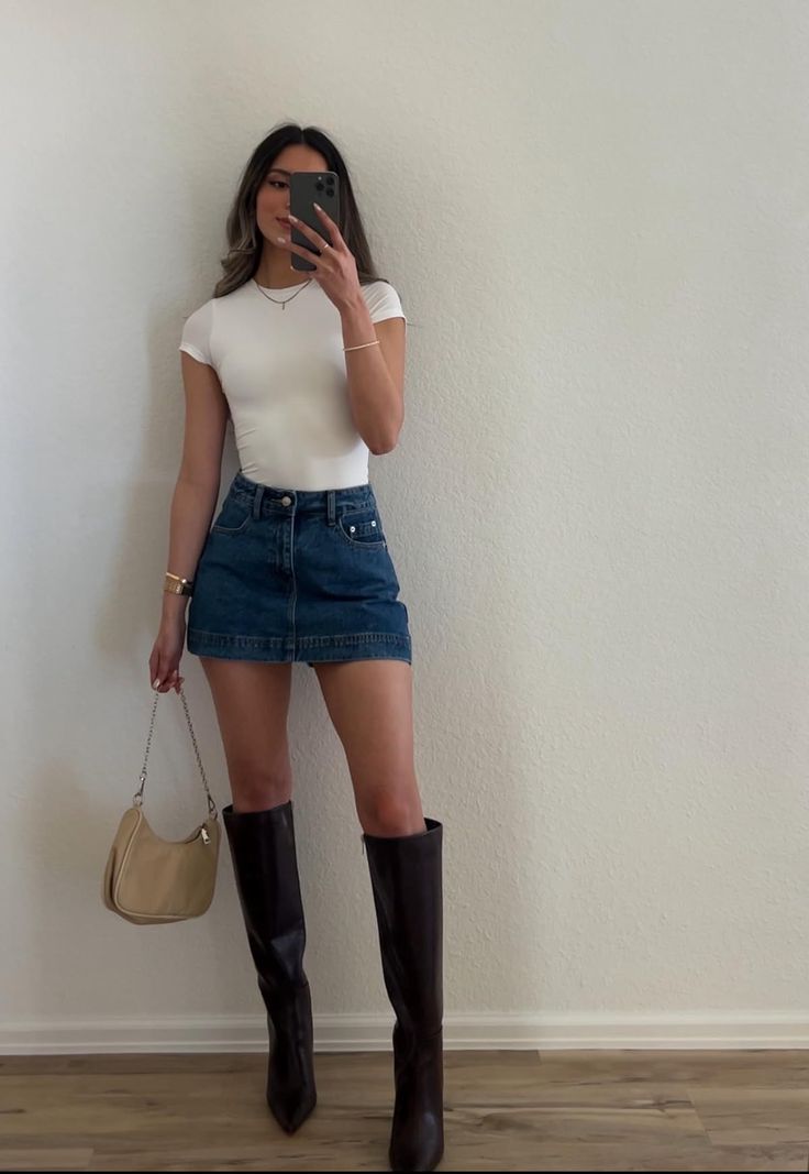 Woman in a white t-shirt and denim skirt taking a mirror selfie