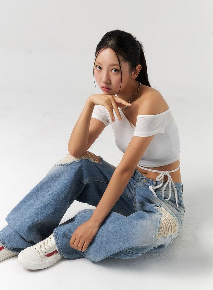 Woman in a white crop top and ripped jeans sitting on a white studio floor