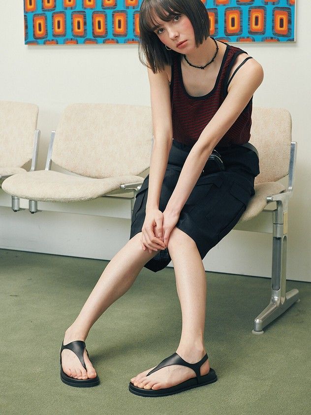 Woman with short hair wearing a striped tank top and black skirt, sitting indoors