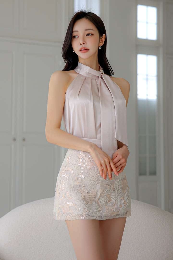 Woman in a light pink halter top and a sequined lace mini skirt indoors