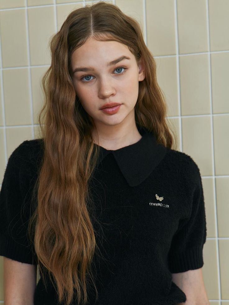 Woman with long wavy hair and blue eyes wearing a black polo shirt indoors