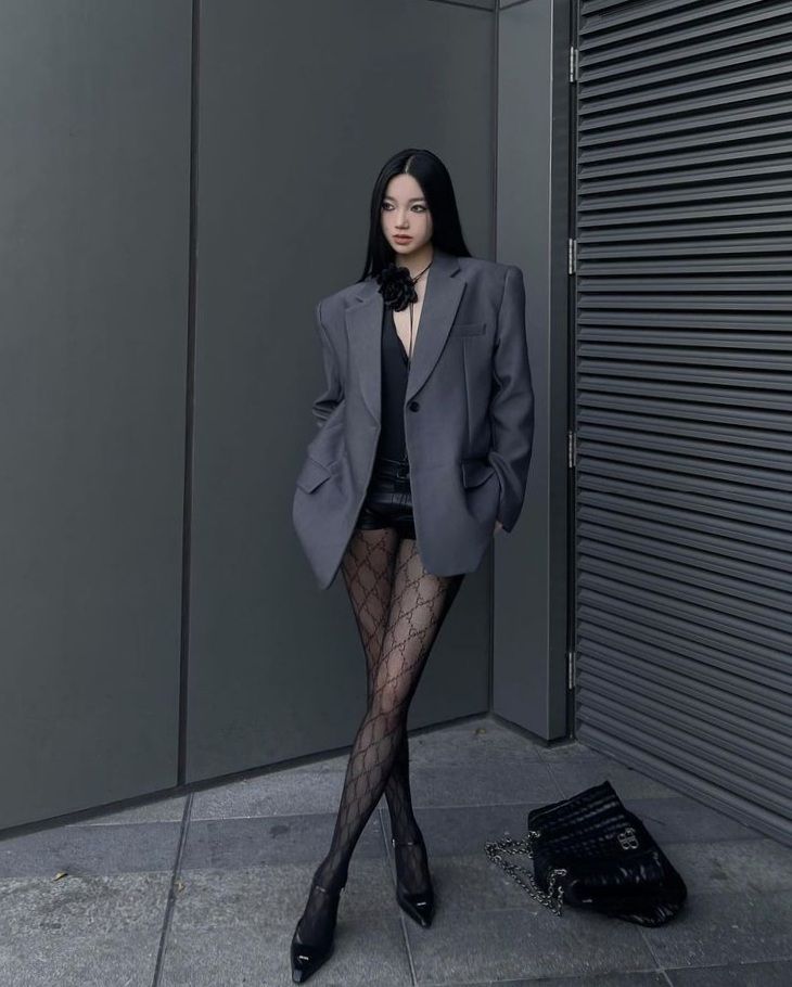 Woman in an oversized blazer and patterned tights posing outdoors