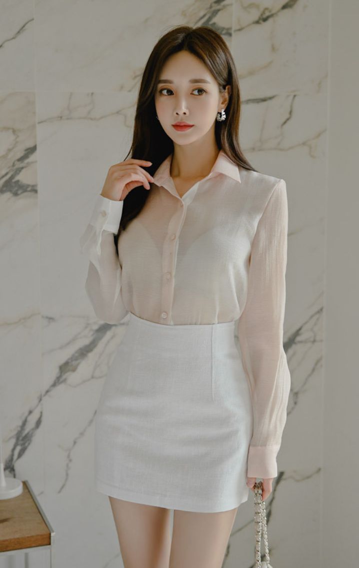 Woman in a sheer shirt and white skirt posing indoors