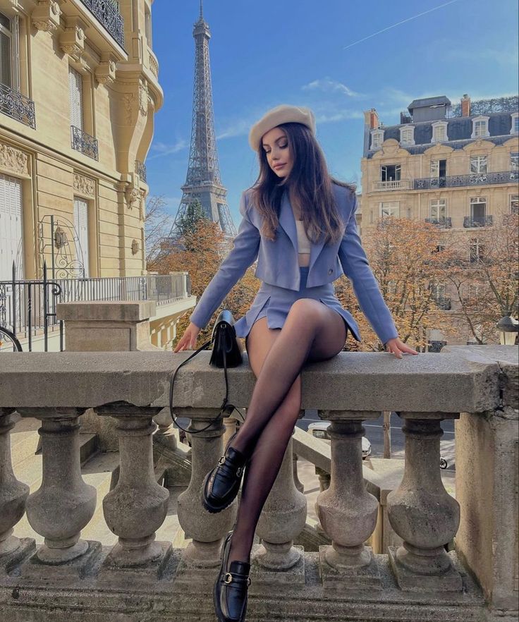 Woman in a blue skirt suit and beret sitting on a stone railing with the Eiffel Tower in the background
