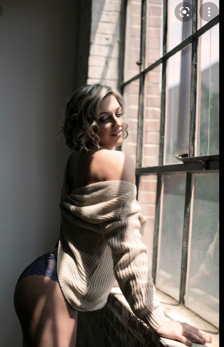 Woman in a sweater and lingerie looking out a window with dramatic lighting