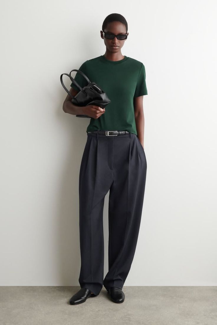 Woman in a dark green t-shirt and wide leg pants holding a black handbag