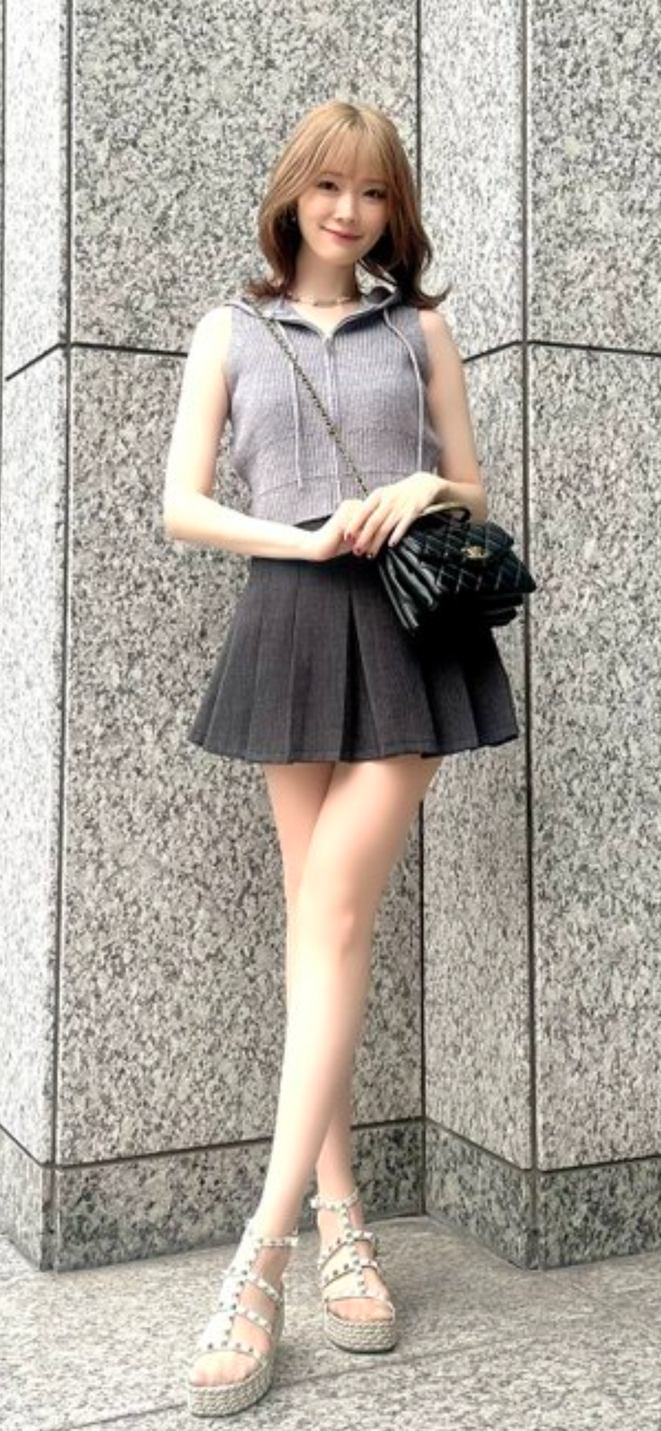 Woman with light brown hair in a pleated skirt and sleeveless top posing outdoors