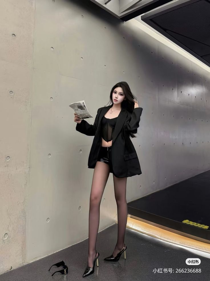 Woman in a black blazer, sheer top, and leather shorts holding a newspaper