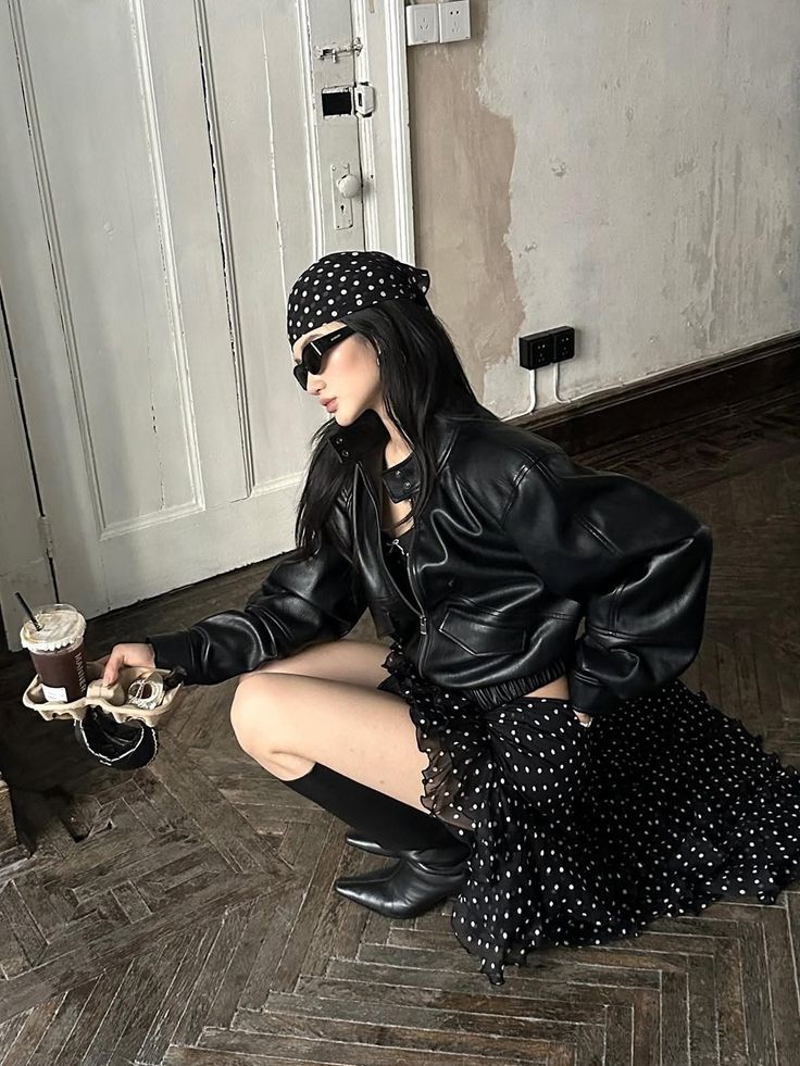 Woman in a leather jacket and polka dot skirt holding drinks, crouching indoors