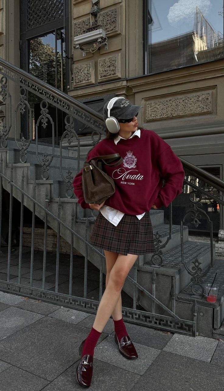 Person in a plaid skirt and burgundy sweatshirt with headphones outdoors