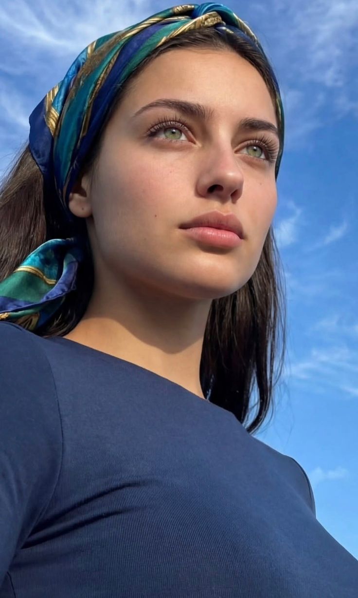 Woman with green eyes and a head scarf looking up at a blue sky