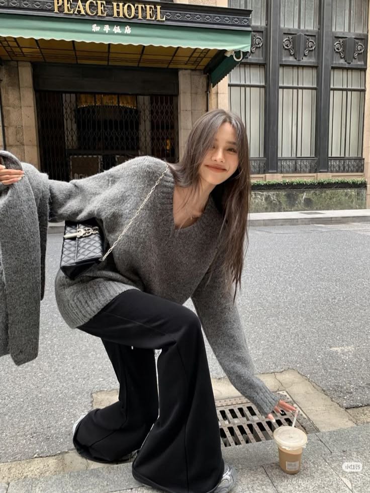Woman in a gray sweater and black pants crouching on a street