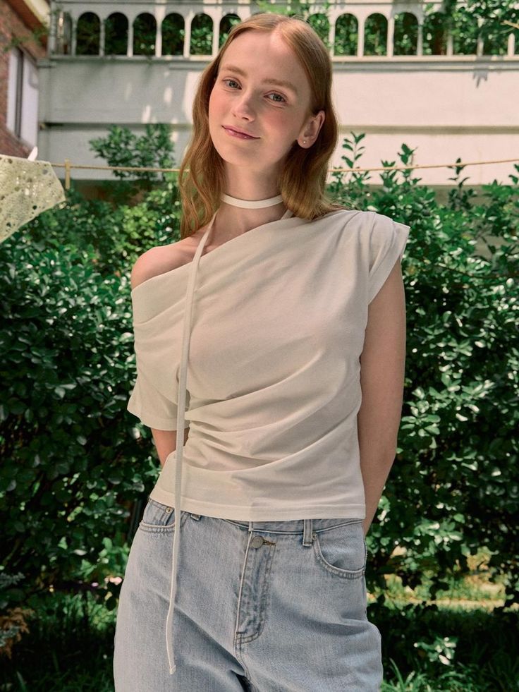 Woman with red hair wearing an off-shoulder top and light wash jeans outdoors