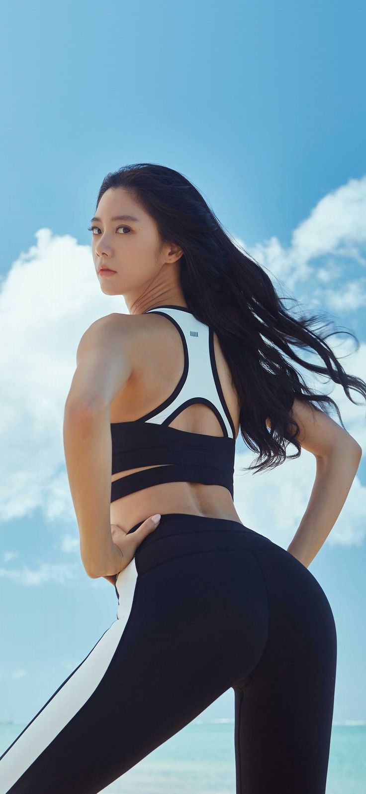 Woman in a sports bra and leggings posing outdoors with a blue sky background