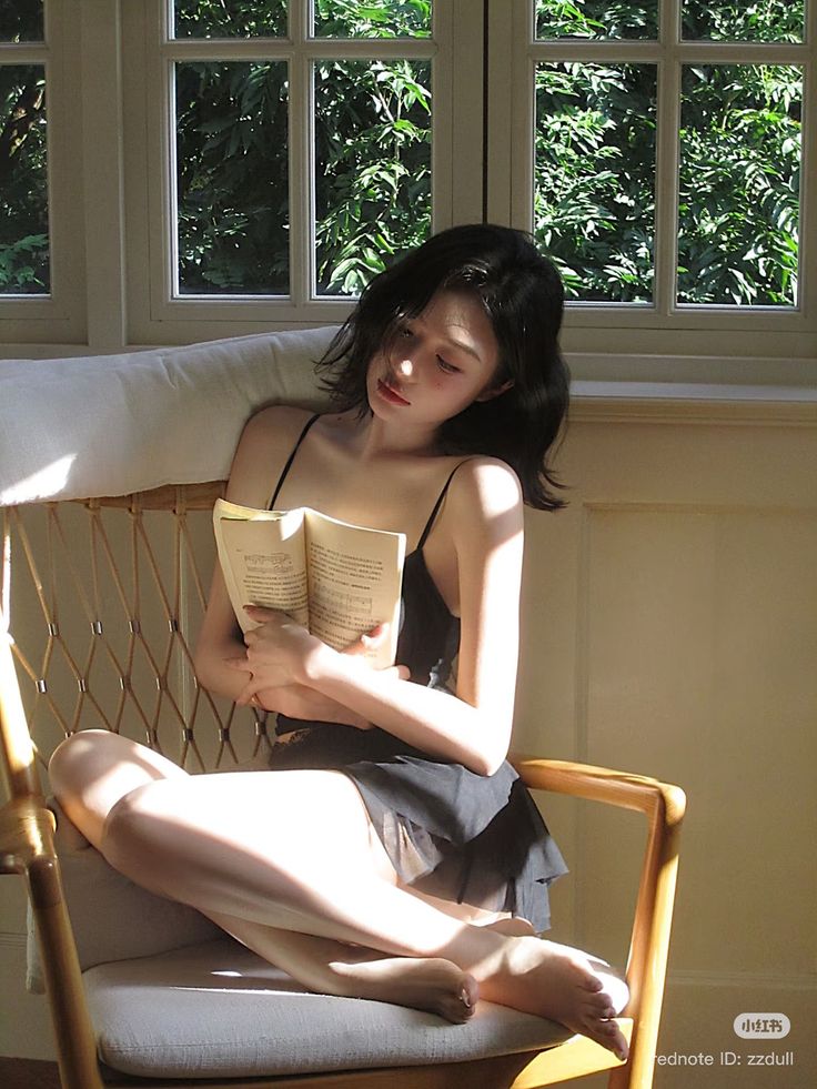 Woman with short black hair reading a book in a sunlit room