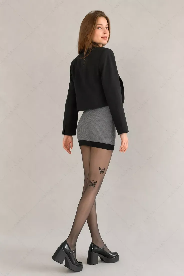 Woman in a black cropped jacket and grey mini skirt with butterfly tights