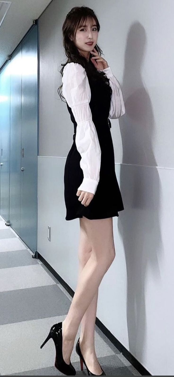Woman in a black dress and white blouse posing indoors