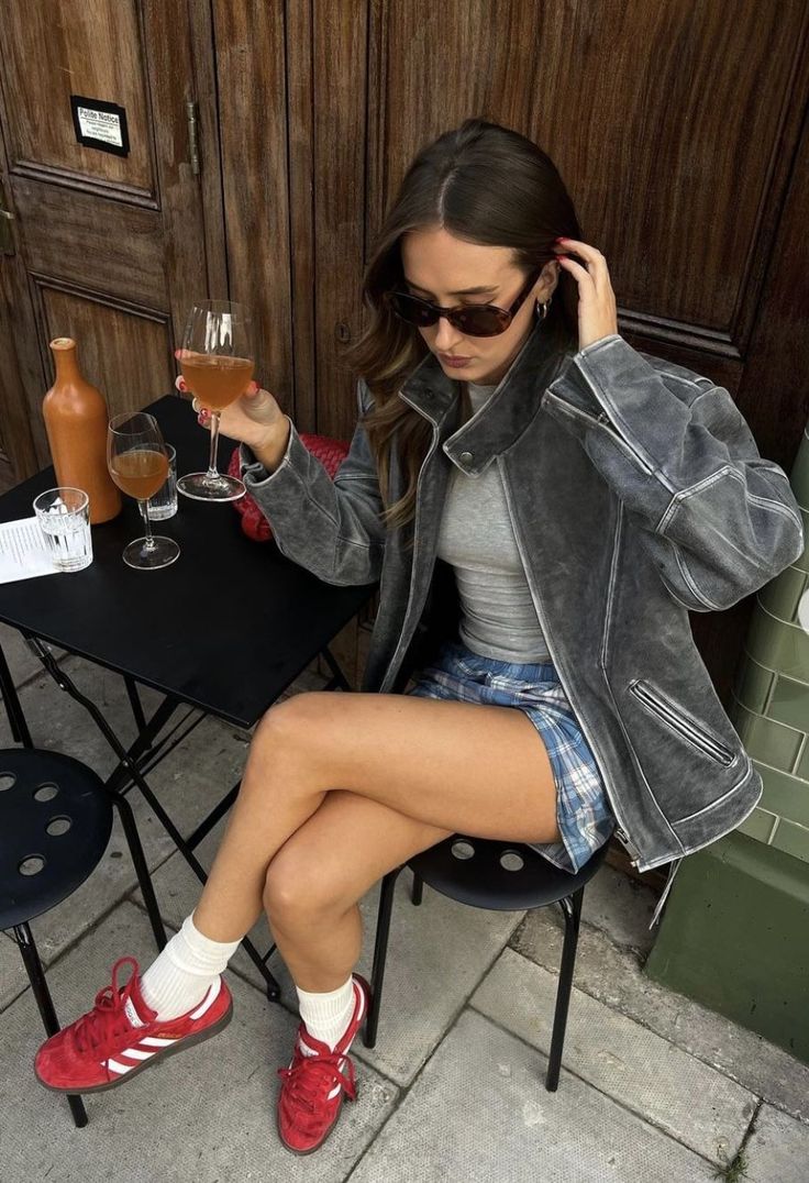 Woman in a leather jacket and plaid skirt sitting outdoors with a drink