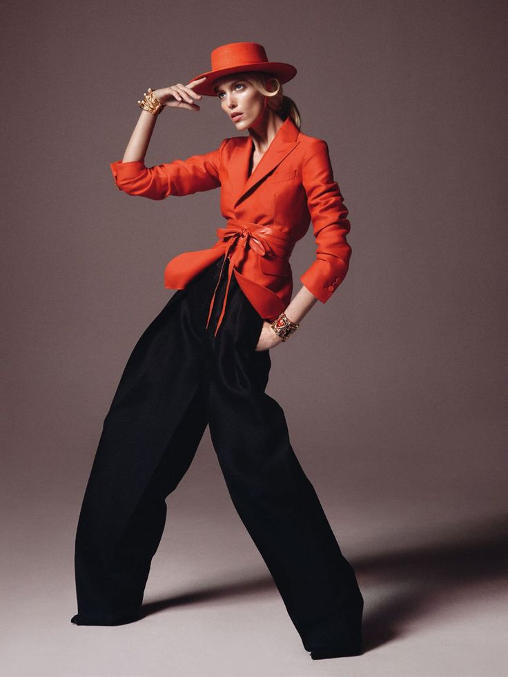 Woman in a red hat and blazer with wide leg pants posing in a studio