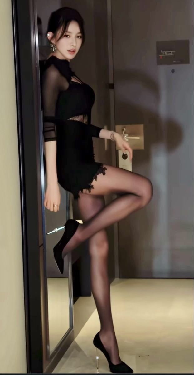 Woman in a black dress and stockings posing indoors