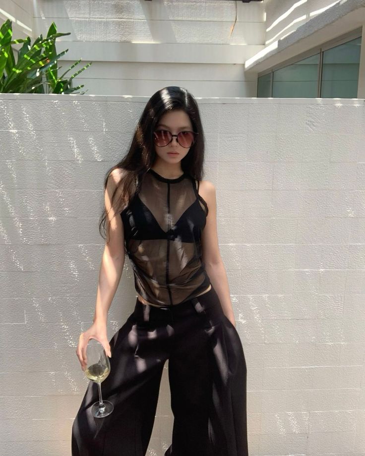 Woman in a sheer top and wide leg pants holding a glass outdoors
