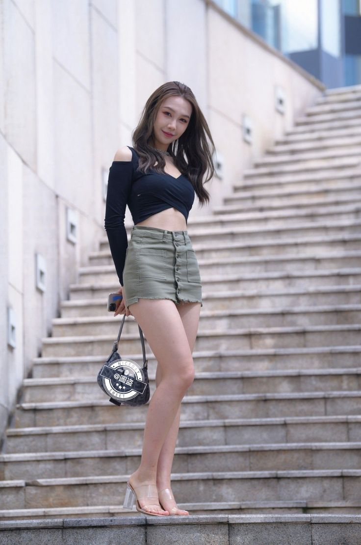 Woman in a black crop top and olive mini skirt standing on outdoor stairs