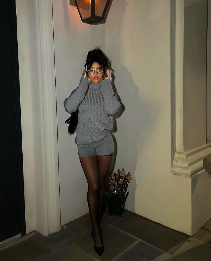 Woman in a gray sweater and shorts with tights and glasses outdoors at night