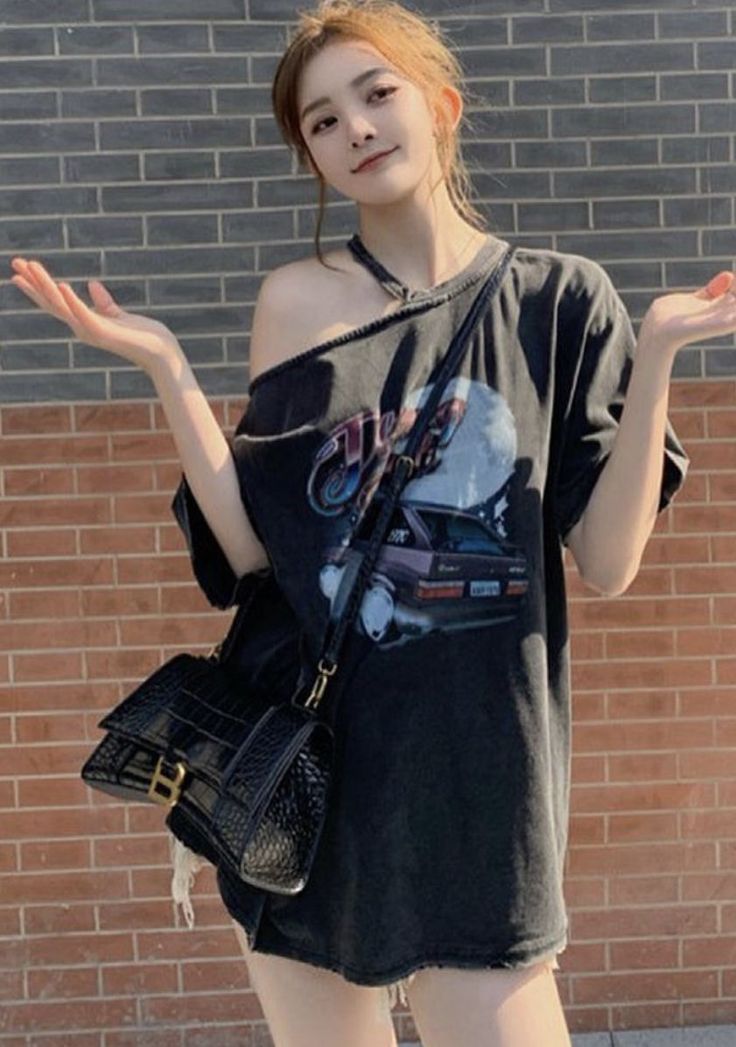 Woman in an off-shoulder top and black handbag against a brick wall