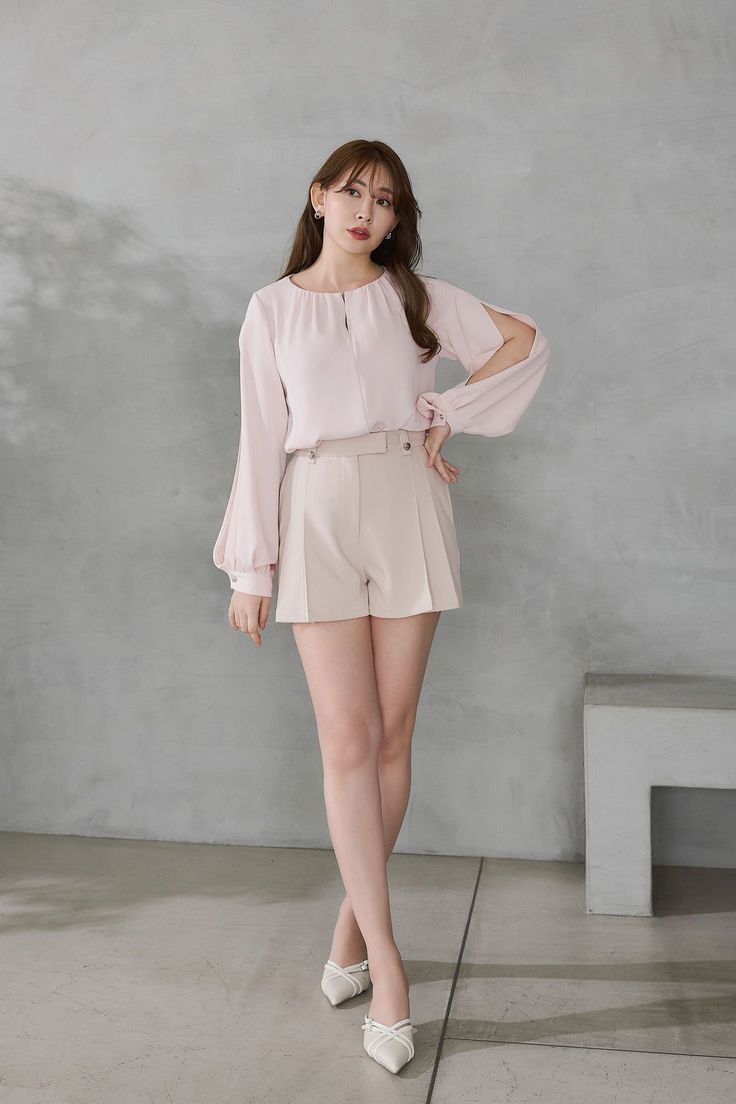Woman in a pink blouse and beige shorts posing indoors